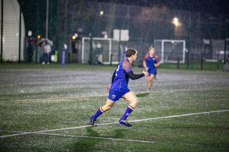 a rugby player running on a pitch while its raining