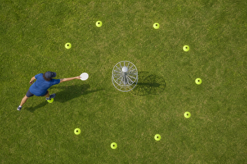 a male adult practicing putting disc golf at a basket in a circle