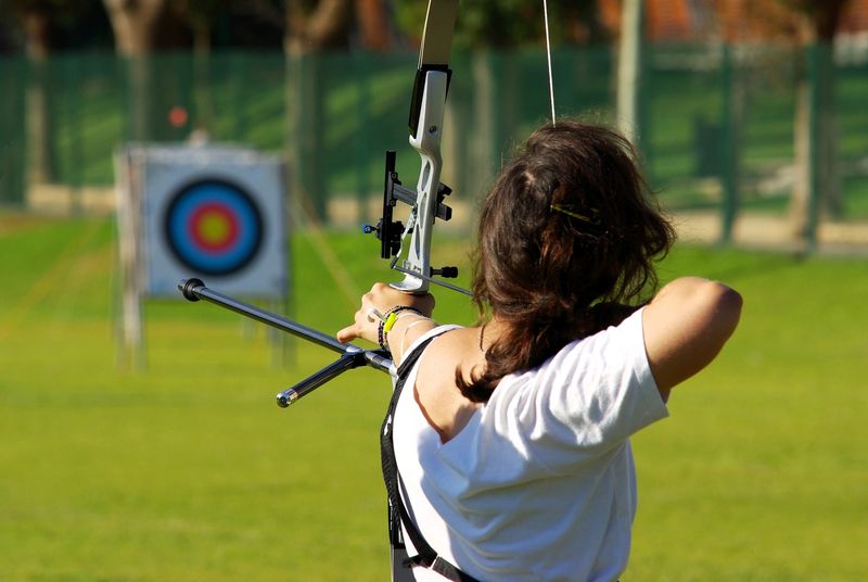 an archer using a black bow to shoot an arrow toward a practice target