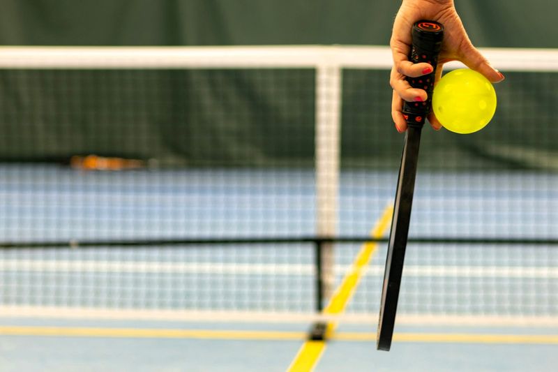 a woman's hand holding a pickleball paddle and pickleball