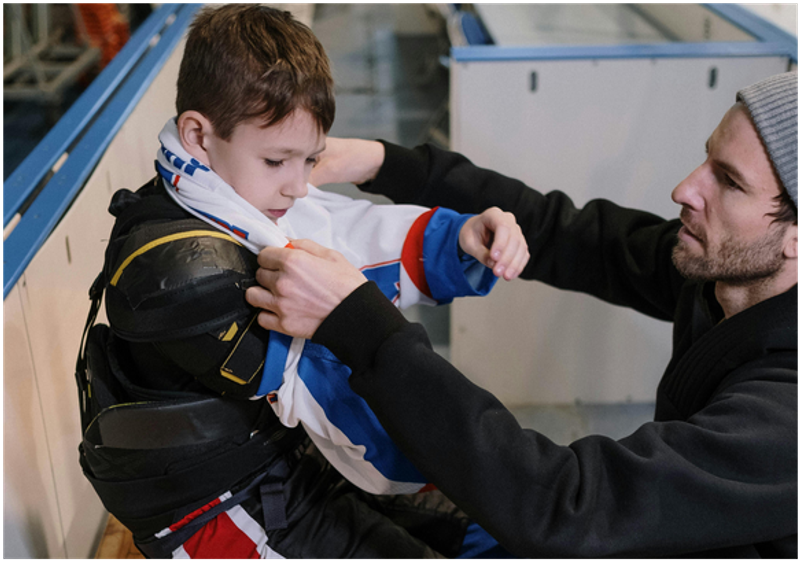 a father helping his child put on hockey gear
