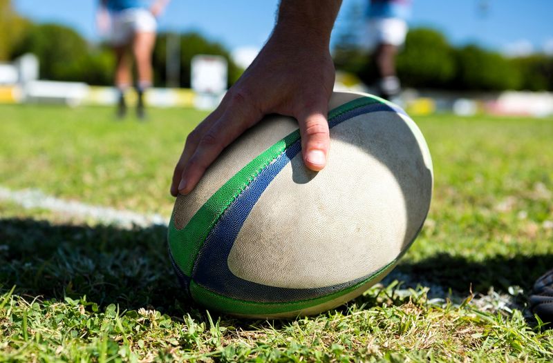 a hand holding a rugby ball on grass