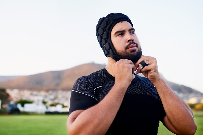 an adult male adjusting the strap on his rugby scrum cap