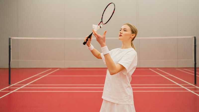 a youth female tossing a shuttlecock into the air