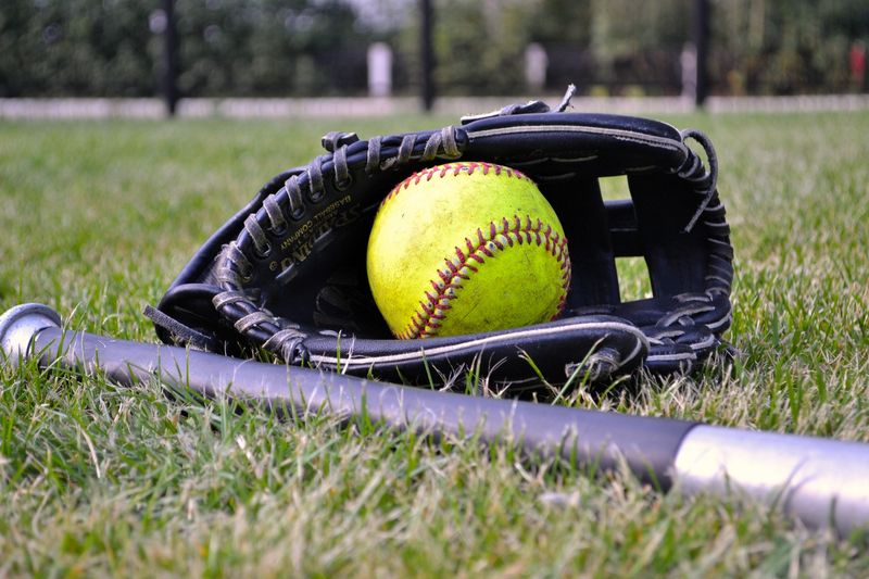 a softball inside a softball glove next to a bat on grass