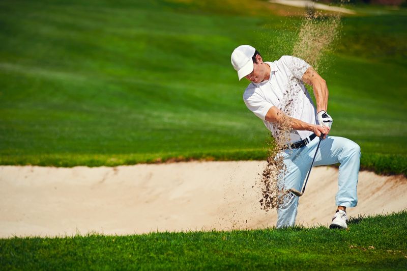 a male adult golfer hitting a golf ball out of a bunker