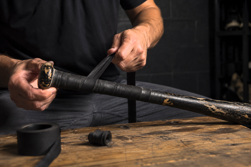 a male adult wrapping a baseball bat handle with bat grip tape