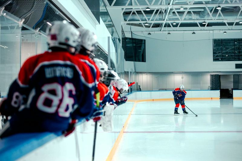 a youth hockey team leaning on an ice hockey rink wall waiting to get onto the ice rink