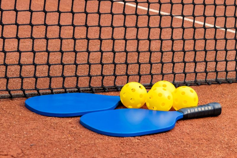 two blue pickleball paddles and 4 pickleballs on an orange pickleball court