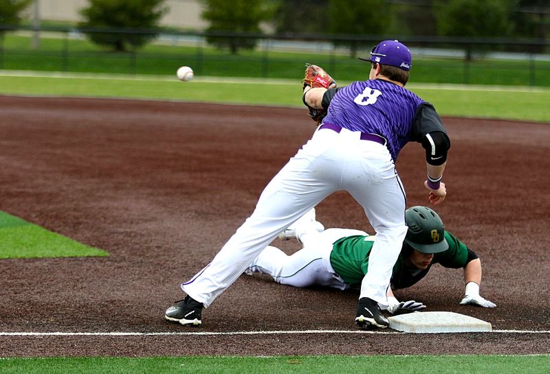 a baseball catcher about to catch a baseball with an opposing player sliding to base