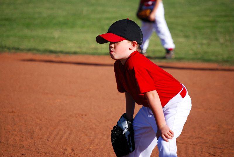 a youth baseball player wearing a red jersey and baseball glove in his right hand