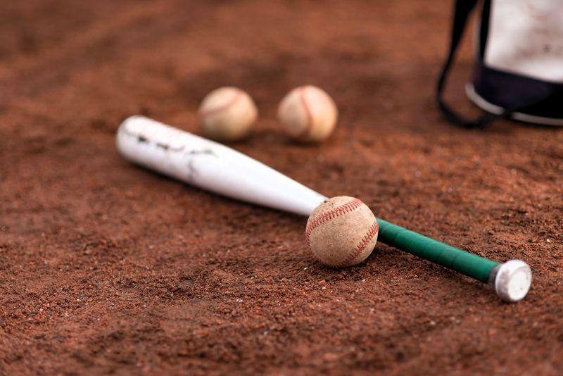 a white baseball bat with green bat grip tape lying on sand next to a white baseball