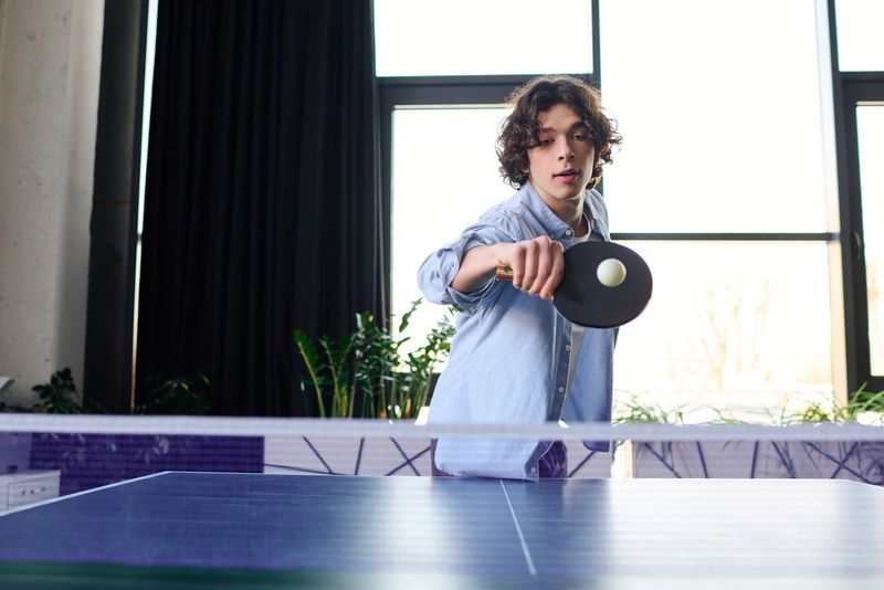 a youth boy playing ping pong using a backhand swing of his racket 