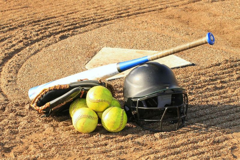 a softball bat on top of softballs and a softball helmet