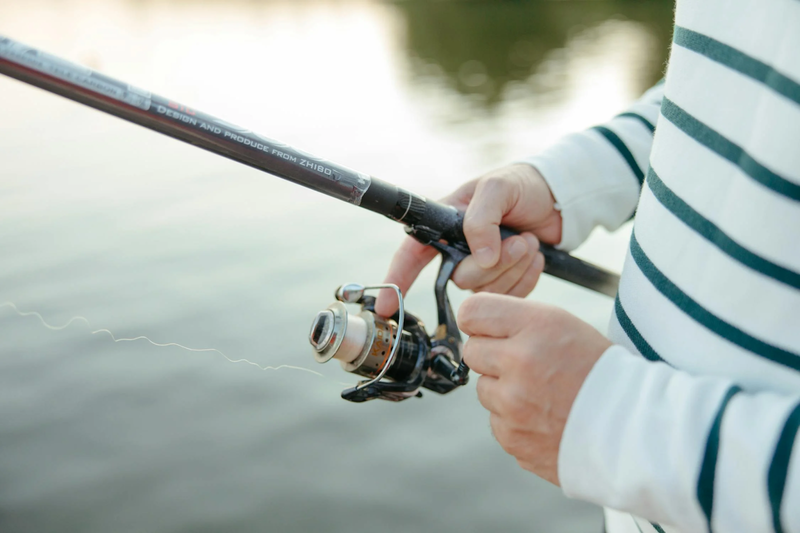 a person holding a fishing rod and reel above a lake