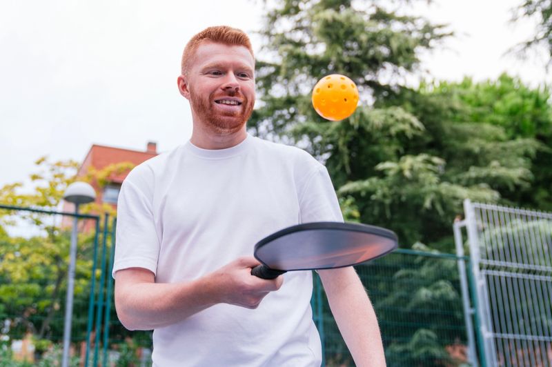 a man bouncing a pickleball on a pickleball paddle