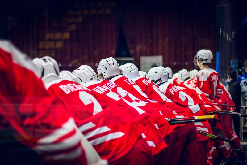 a hockey team wearing red uniform leaning over an ice hockey rink wall