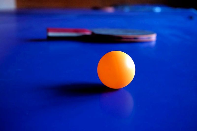 an orange ping pong ball with a ping pong paddle in the background