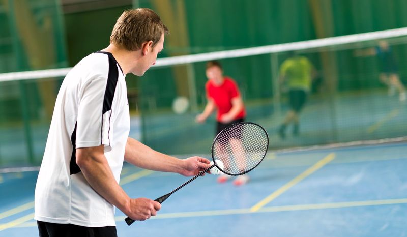 a badminton player about to serve a shuttlecock to an opponent