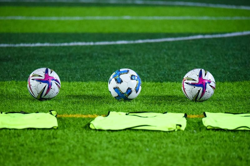 three soccer balls on grass behind green pinnies