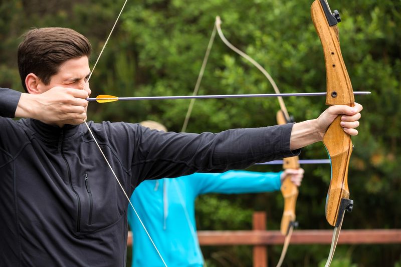 a male archer aiming a wooden bow before shooting an arrow