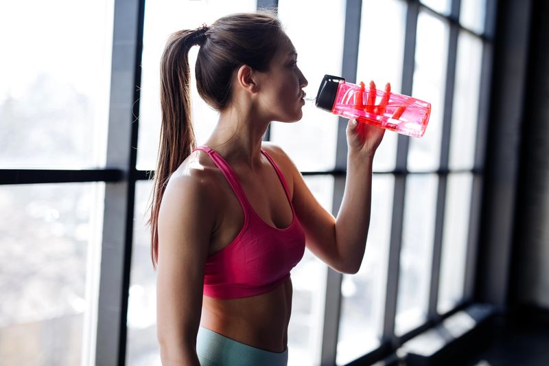 an adult female drinking from a sport water bottle in gym studio