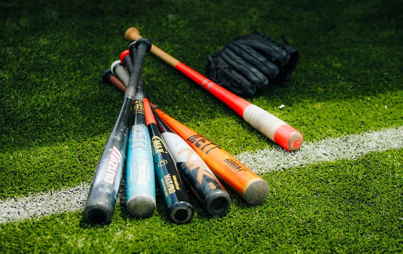 multiple baseball bats lying on a grass field next to a catchers mitt