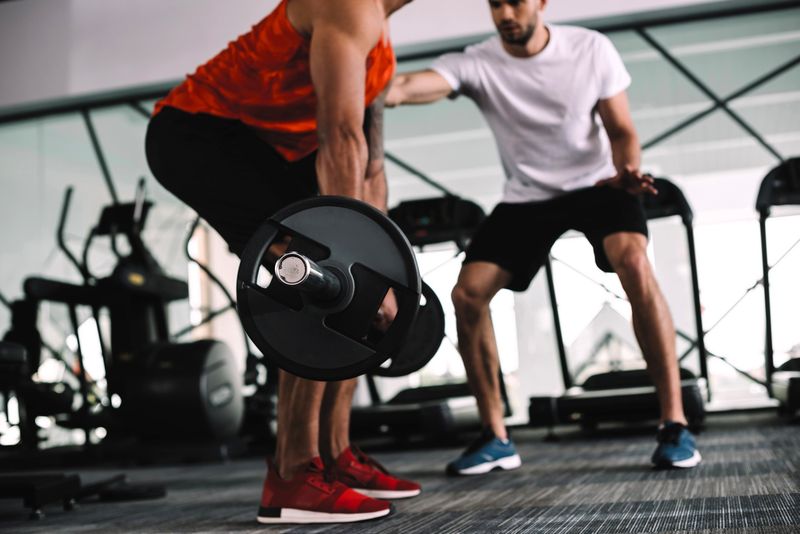 a man doing deadlifts next a trainer in a gym