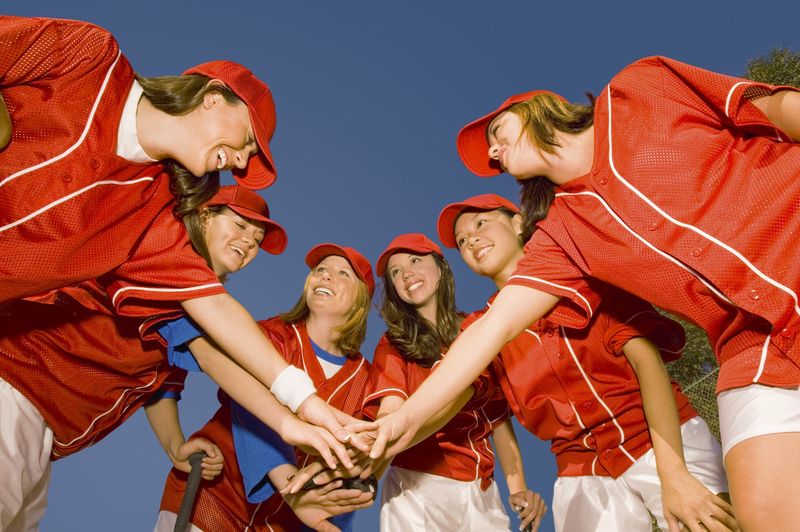 a female softball team putting their hands together