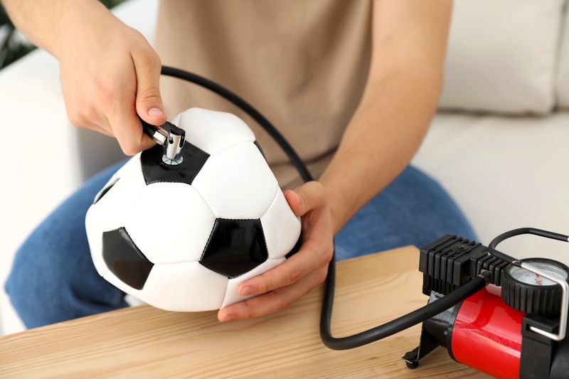 a male adult inflating a soccer ball using a pump