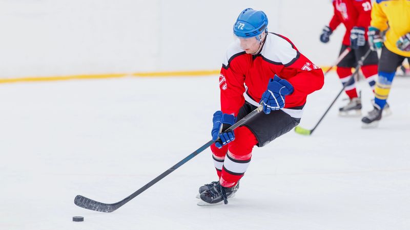 a male adult hockey player wearing a red hockey uniform skating on ice