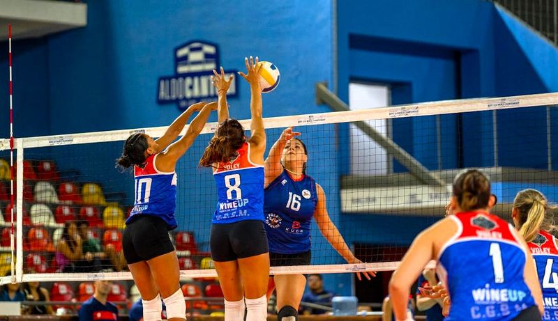 two volleyball teams jumping on either side of a volleyball net