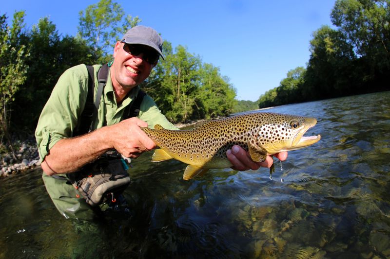 a male fisherman in a river holding a trout