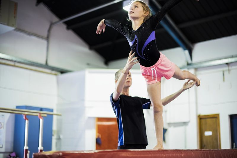 a gymnastics instructor helping a gymnast on a balance beam