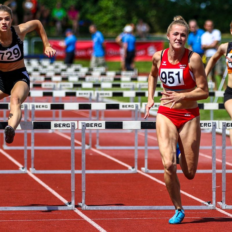 3 adult female track athletes jumping hurdles on a running track