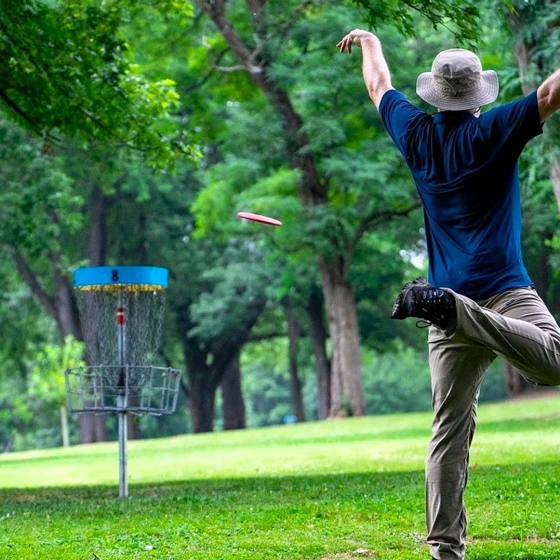 an adult man after throwing a disc golf disc at a bucket