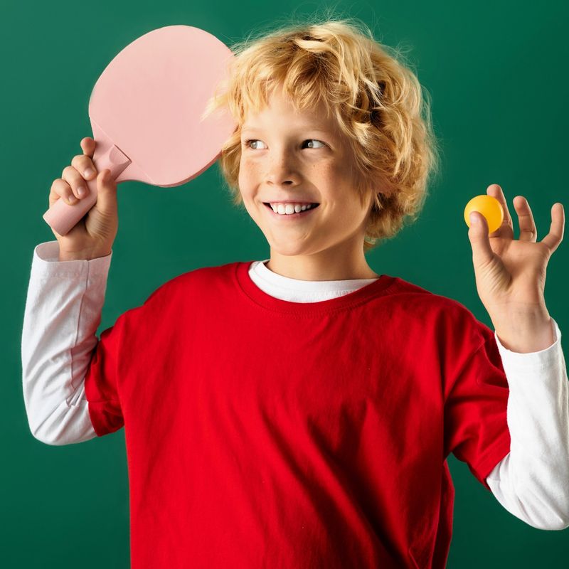 a youth boy holding a pink ping pong paddle and a ping pong ball