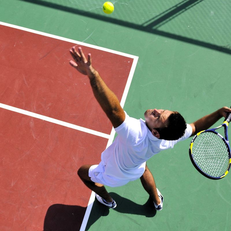 a male adult tennis player tossing a tennis ball before a serve