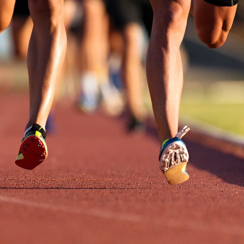 two track athletes running a running track wearing spike shoes