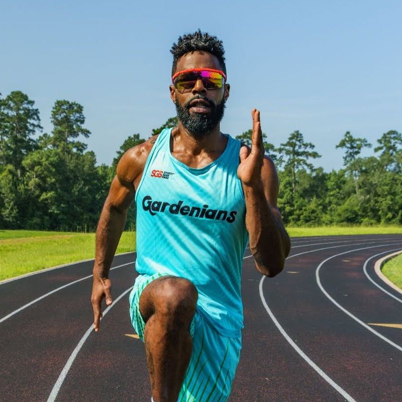 a male adult track and field athlete wearing a blue uniform on an outdoor running track