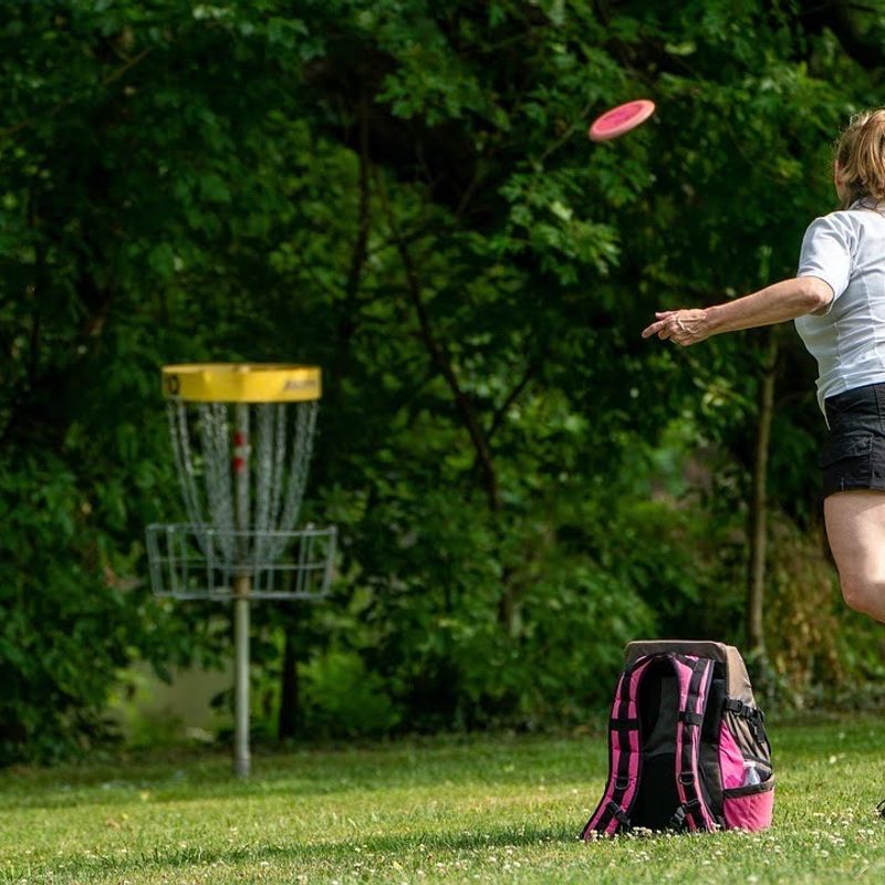 an adult female throwing a disc golf at a basket