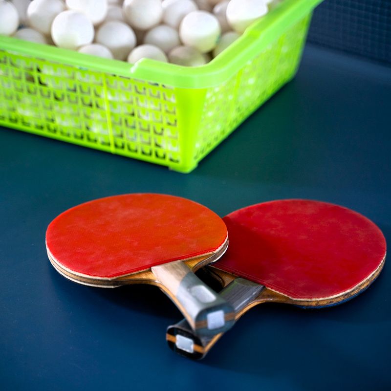 two ping pong paddles next to a basket of ping pong balls