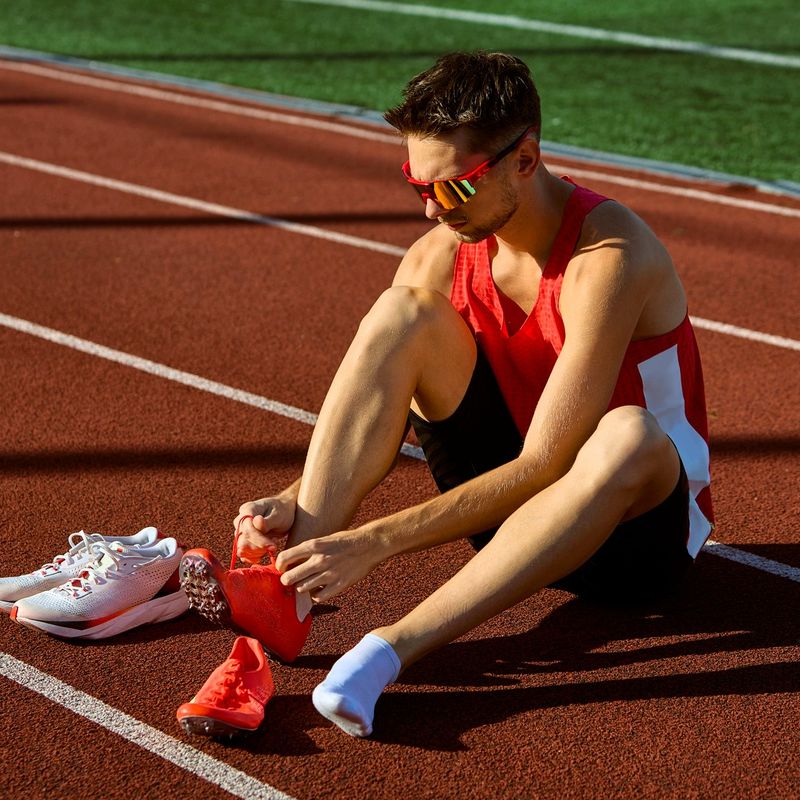 a male adult track athlete putting on track shoes next to a pair of running shoes