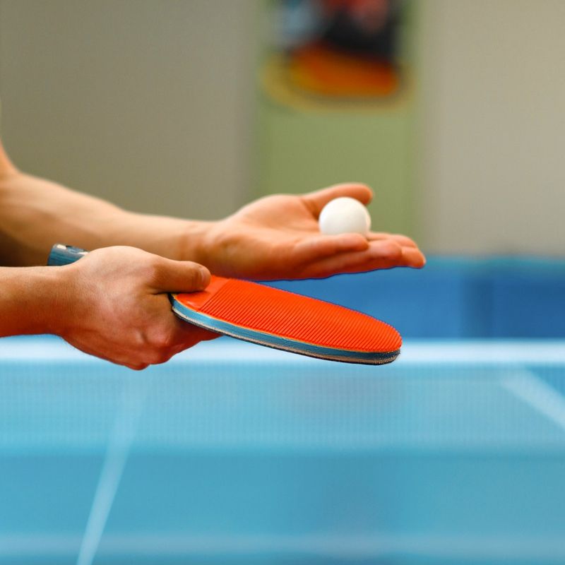 an adult male holding ping pong paddle and a white ping pong ball