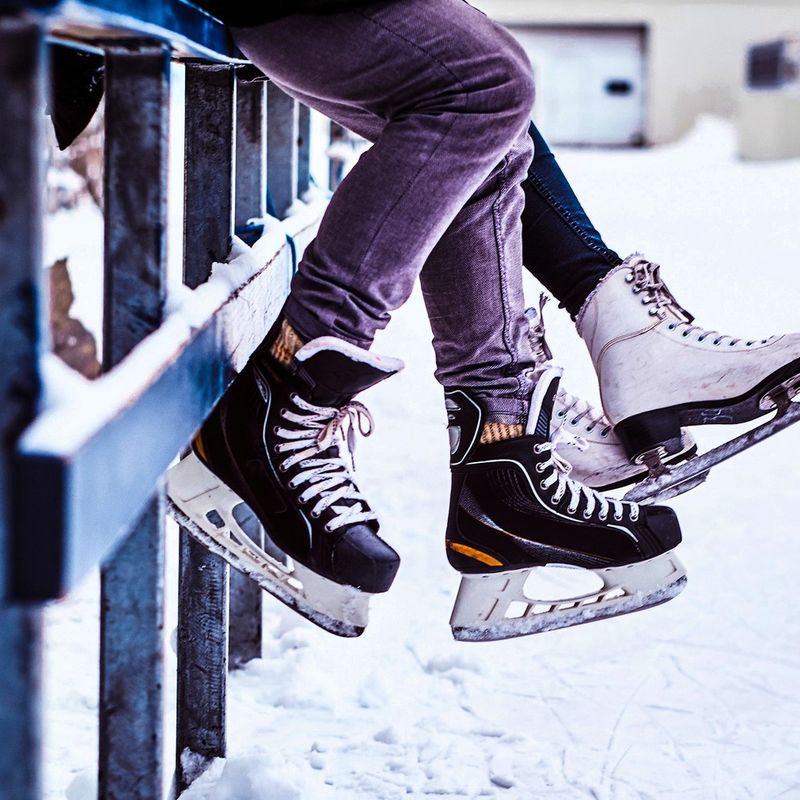 two people sitting on a wooden fence wearing ice skates and hockey skates
