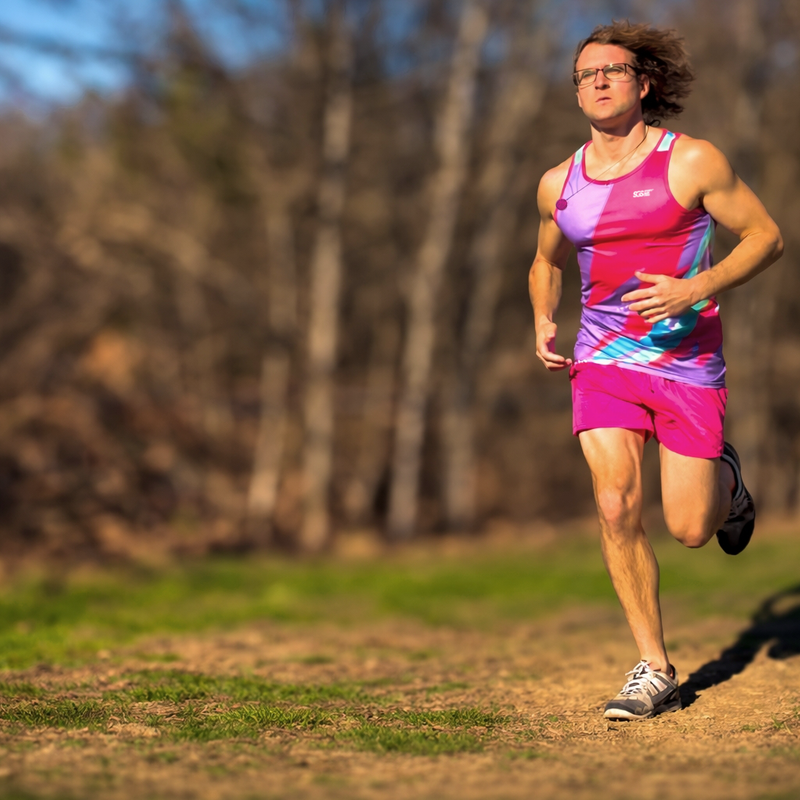 a male adult track athlete running on grass in front of a forest